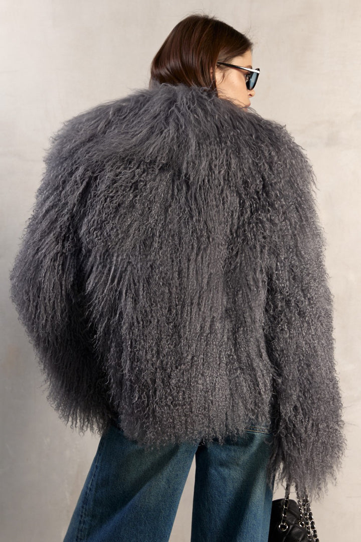 A woman dressed in a handcrafted grey Mongolian fur coat, showcasing long sleeves, a dramatic collar, and a refined silhouette with satin and leather lining for a sophisticated look.